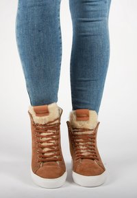 Ruske nubuk høye sneakers med pelsfôr, hvit gummisåle og brune lisser. Har en merkepatch i lær på tungen.