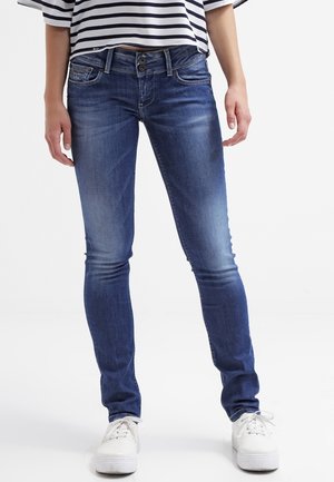 Jeans ajustados en denim de lavado medio, con un diseño clásico de cinco bolsillos, un ligero desgaste y presillas para cinturón, combinados con zapatillas blancas.