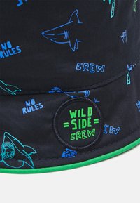 Svart stoffbøttehatt med blå hai- og "No Rules" grafikk, med en grønn-accentuert skjerm og en sirkulær "Wild Side Crew" logo-patch.