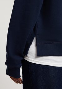 Granatowa bluza z ribbowanymi mankietami i dołem, z bocznym rozcięciem. Nosi się ją na białej koszulce i ciemnoniebieskich dżinsach, co ukazuje kontrast tekstur.