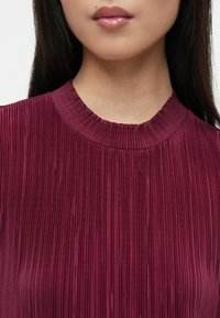 Βουργουνδίας πλισέ τοπ με υφή και ριμπ κολάρο, με λεπτές κάθετες γραμμές σε όλη την ύφασμα.