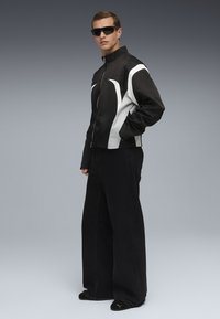Sort og hvid lynlåsjakke med en tætsiddende pasform, parret med brede sorte bukser og sorte slip-on sko. Minimalistisk stil og tekstur.