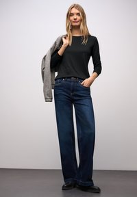 Czarny długi rękaw, wyblakłe niebieskie szerokie jeansy, szary kardigan zarzucony na ramię, czarne obuwie, minimalistyczny design, gładka tekstura.