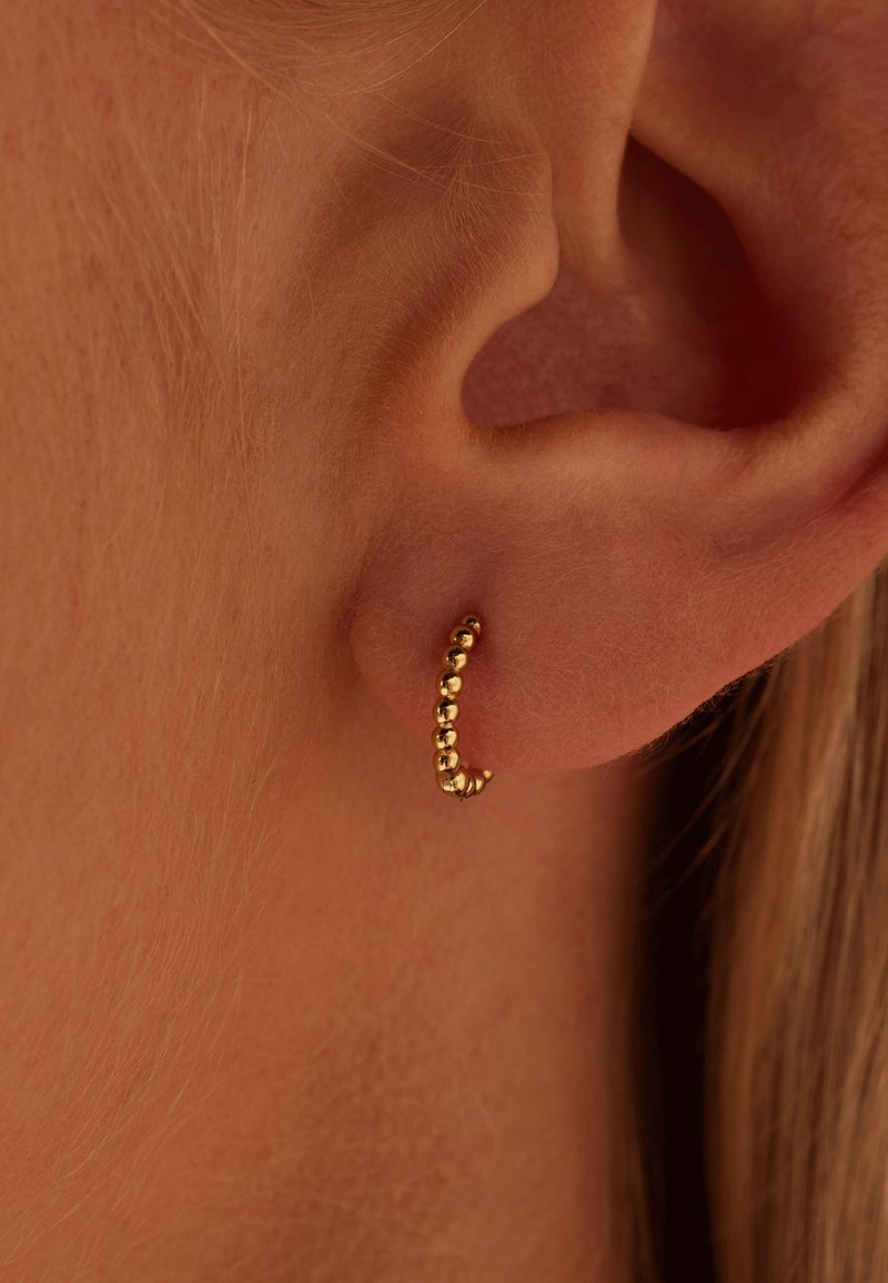 Boucle d'oreille en or avec un design courbé et de petites perles rondes. La texture est lisse et brillante, complétant le contour de l'oreille.