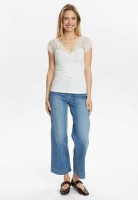 Top blanco de canalé con mangas cortas de encaje, escote en V, combinado con jeans de mezclilla de pierna ancha azul claro y zapatos marrón oscuro.