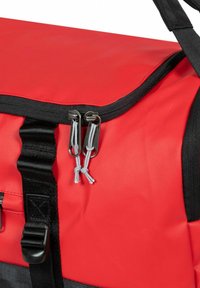 Sac de sport en polyester rouge avec une fermeture éclair noire et des tirettes en argent, des cordons de tirage gris et des sangles en toile noires pour le transport.