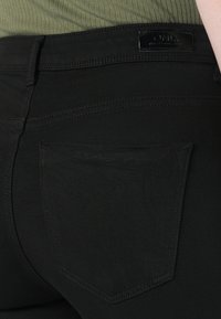 Schwarze Jeans aus Denim mit strukturierter Oberfläche, ausgestattet mit einer Gesäßtasche und einem Leder-Brandlabel. Das Design beinhaltet feine Steppnähte.