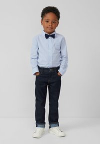 Blauw en wit gestreepte button-up shirt, donkere spijkerbroek en witte sneakers. Bevat een marineblauwe vlinderdas en opgerolde mouwen.
