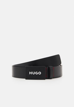 Schwarzer Ledergürtel, aufgerollt mit rechteckiger schwarzer Schnalle, die weißen "HUGO"-Text und rote Naht in der Nähe der Gürtelschlaufe zeigt.