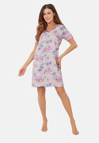 Koszula nocna z krótkim rękawem w jasnoróżowym kolorze z kwiatowym wzorem w odcieniach niebieskiego i fioletowego. Posiada dekolt w kształcie litery V oraz długość do kolan.