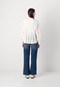 White, long-sleeve blouse with pleats at the back, paired with wide-leg blue jeans and light-colored shoes. Smooth texture, simple design.