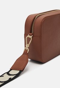 Bruine leren tas met textuur, gouden ritssluiting, rechthoekige vorm en afneembare zwart-wit patroonriem.