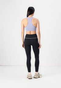 Light purple ribbed sports bra with racerback design paired with high-waisted black leggings featuring a reflective accent. Neutrals shoes.