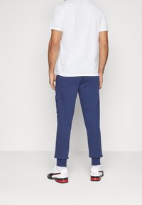 Weißes T-Shirt mit kurzen Ärmeln, marineblaue Jogginghose mit Seitentasche und schwarz-weiße Sportschuhe mit roten Akzenten.