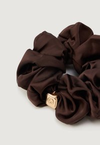 Scrunchie em cetim castanho com um design texturizado e franzido. Apresenta acessórios em tom dourado com um detalhe de logo em relevo.