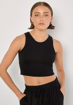 Schwarzes, kurzes Tanktop aus geripptem Material mit einem runden Ausschnitt und breiten Schulterträgern. Kombiniert mit schwarzen Jogginghosen mit Kordelzug.