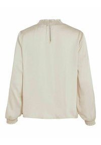 Blouse couleur crème avec manches longues, encolure froncée et poignets élastiques. Texture lisse, fermeture éclair au dos.