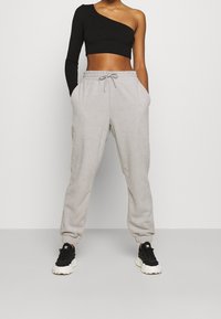 Schwarzes, einseitiges, geripptes Cropped-Top, kombiniert mit hellgrauen Fleece-Sweatpants mit Kordelzug und Knöchel-Bündchen. Getragen mit schwarzen Sneakers.