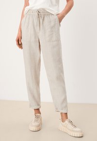 Ljusbeige linnebyxor med elastisk midja och dragsko, med två framfickor och uppvikta muddar. I kombination med klumpiga beiga sneakers.