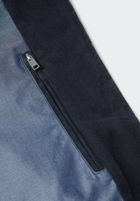 Gros plan sur une fermeture éclair noire sur une poche en tissu bleu avec des bordures noires, montrant les coutures détaillées et la texture des matériaux.