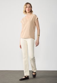 Beige short-sleeve V-neck top paired with cream straight-leg pants and black flat shoes, featuring a smooth texture and minimal design.