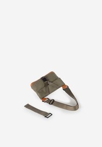 Olivengrüne crossbodytas met een bruine leren accent, verstelbare riem en gesp sluiting. Gestructureerd materiaal met een compacte vorm.