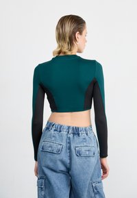 Teal en zwarte cropped longsleeve top met een aangesloten ontwerp, gecombineerd met lichtblauwe cargobroek met zijzakken en een elastische taille.