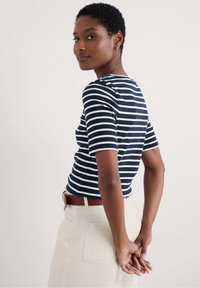 Navy and white striped ribbed top with short sleeves, paired with light-colored high-waisted pants and a brown belt. Simple, fitted design.