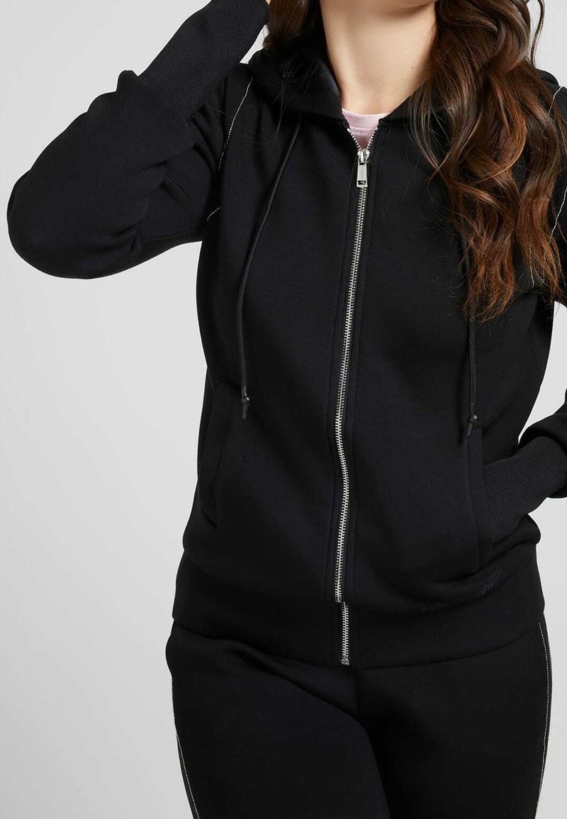 Svart zip-up hoodie tillverkad av mjukt tyg, med en justerbar huva, sidofickor och kontrasterande sömnadsdetaljer.