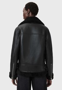 Czarna skórzana kurtka z kołnierzem z owczej wełny, z zamkami błyskawicznymi na mankietach i gładkim wykończeniem. Projekt jest dopasowany w klasycznej sylwetce.