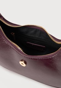 Σκούρα μοβ δερμάτινη τσάντα χειρός ανοικτή, που αποκαλύπτει το εσωτερικό από μαύρο ύφασμα με μια τσέπη με φερμουάρ και κούμπωμα με χρυσό μαγνητικό κούμπωμα.