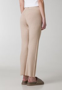 Beige geribbelde gebreide broek met een uitlopende pijpdesign en een elastische tailleband. Bevat een klein logo-label aan de achterkant. Zachte textuur.