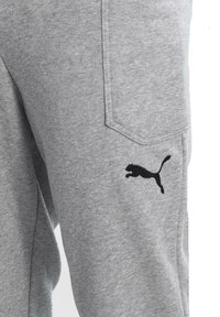 Hellegraue Sweatpants aus weichem Material, mit einem schwarzen Puma-Logo auf dem linken Bein und einer Seitentasche. Schlichtes Design mit bequemer Passform.