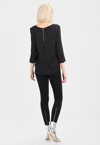 Top negro estampado con mangas tres cuartos, presenta una pequeña cremallera en la parte posterior. Combinado con pantalones ajustados negros y botas de tobillo plateadas brillantes con cremalleras.