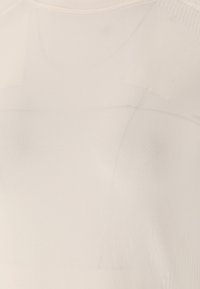 Ljust beige åtsittande topp gjord av mjukt, slätt tyg. Har en rund halsringning och subtila ribbningar längs axelsömmarna.