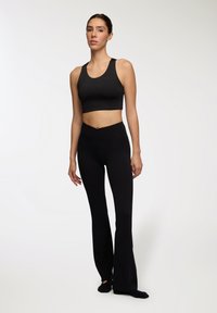 Top sportivo nero a maniche corte con scollatura tonda abbinato a leggings neri a vita alta e a campana; entrambi realizzati in un tessuto liscio e elastico.