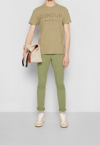 Khakifärgad t-shirt med blekt logotyp, ljusgrön slim-fit byxor och beige väska med rullad flap. Vita sneakers med krämfärgade detaljer.