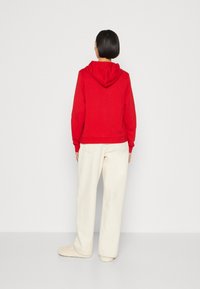 Sudadera roja con cordón, con dobladillo y puños acanalados, combinada con pantalones holgados de color crema y zapatillas beige.