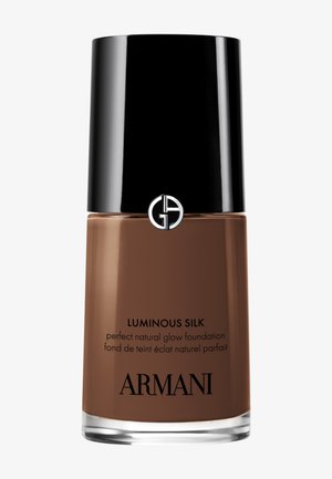 Luminous Silk foundation i en klar glassflaske med sort lokk og logo, som viser en middels brun væske inni.