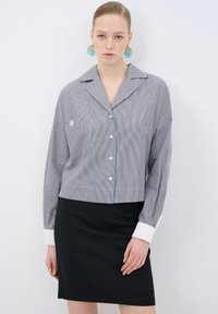 Kaproppad skjorta med knappar i svart och vitt randigt mönster, med bröstficka, markerad krage och vita manschetter, kombinerad med en svart kjol.