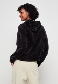 Felpa nera corta realizzata in materiale morbido e peloso. Presenta un cappuccio e maniche con vestibilità rilassata, con cuciture minime e senza hardware visibile.