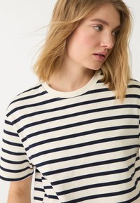 Hvid bomulds T-shirt med marineblå vandrette striber, rund halsudskæring, korte ærmer og afslappet pasform. Blød tekstur, minimale syninger.