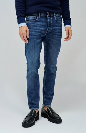 Jeans azul oscuro de corte slim, con un ligero desgastado y arrugas sutiles. Combinados con mocasines negros y un suéter navy con acentos azules.