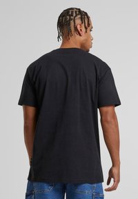 Černé bavlněné tričko s krátkým rukávem, volným střihem a rovním lemem. Významným detailem je duhová nášivka na lemu.