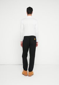 Mustad püksid elastse vöökohaga, kombineeritud valge pika varrukaga särgiga. Inimene kannab tan-toonilisi saapaid, mis on nähtavad tagantpoolt.