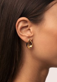 Pendientes de lágrima de oro con un acabado pulido, que presentan un diseño de corte abierto y bordes suaves, complementando la forma de la oreja.