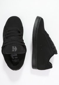 Schwarze Sneakers mit einem glatten Obermaterial aus Stoff, Schnürverschluss, gepolstertem Kragen und Gummisohle. Minimalistisches Design mit dezentem Branding.