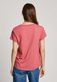 Chemise à manches courtes en tissu corail doux. Coupe décontractée avec un col rond et un ourlet légèrement arrondi. Texture en coton. Aucun motif visible.