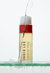 AHA Exfoliating Solution bottle with a transparent body, red cap, and black text, surrounded by splashing water against a white background.