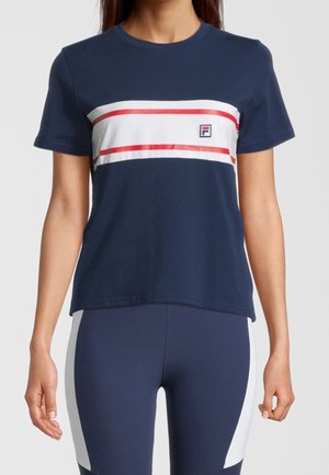 Kobieta ubrana w granatową koszulkę z krótkim rękawem z poziomymi białymi i czerwonymi paskami oraz granatowe legginsy z białymi bocznymi panelami.